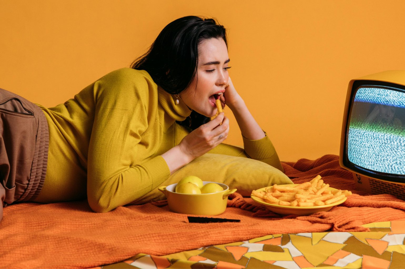 Woman in Yellow lying in bed and eating chips and lemons, watching the TV